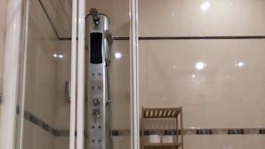 Un box de ducha con paredes de azulejos, un panel de control y un estante de madera.