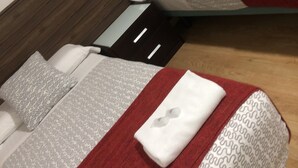 Una cama con cabecera de madera, ropa de cama con estampado gris y una colcha roja.