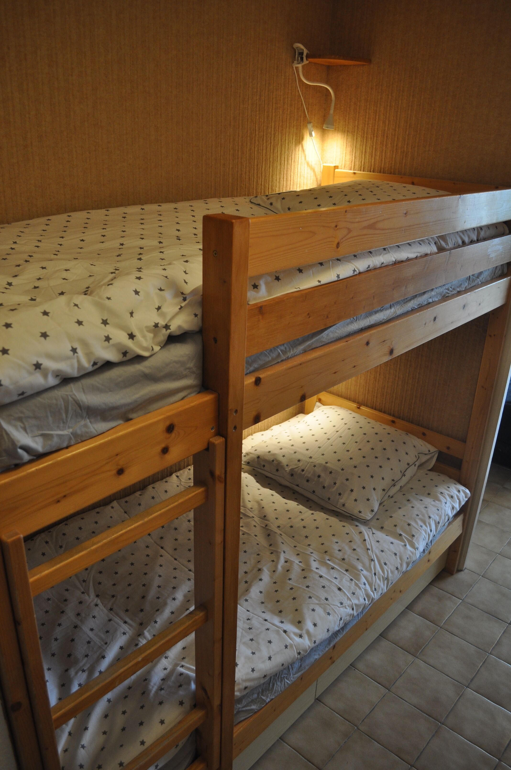 A bunk bed with a wooden frame and a wall-mounted reading light.