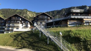 Un hotel con varios balcones, un cartel de alquiler de esquíes y tablas de snowboard, y un telecabina al fondo.