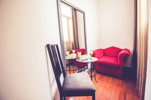 A small room with a red sofa, a chair, a small table with books and glasses of orange juice, and a large mirror.