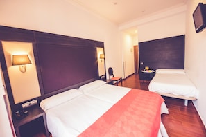 A hotel room with two beds, a desk, a chair, and a small table with a fruit basket. - Hostal Sol Los Angeles (Madrid)