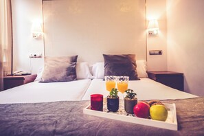 Habitación de hotel con una cama, dos lámparas de noche, un teléfono junto a la cama y una bandeja con frutas y vasos de jugo.