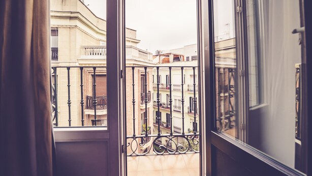 Vista da un balcone con ringhiera in ferro battuto, su una fila di edifici con balconi e cielo sereno.
