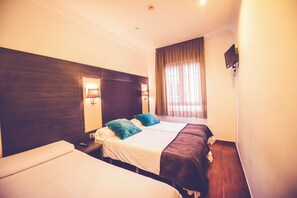 Habitación de hotel con dos camas individuales, un ventanal grande con cortinas y un televisor de pantalla plana montado en la pared.