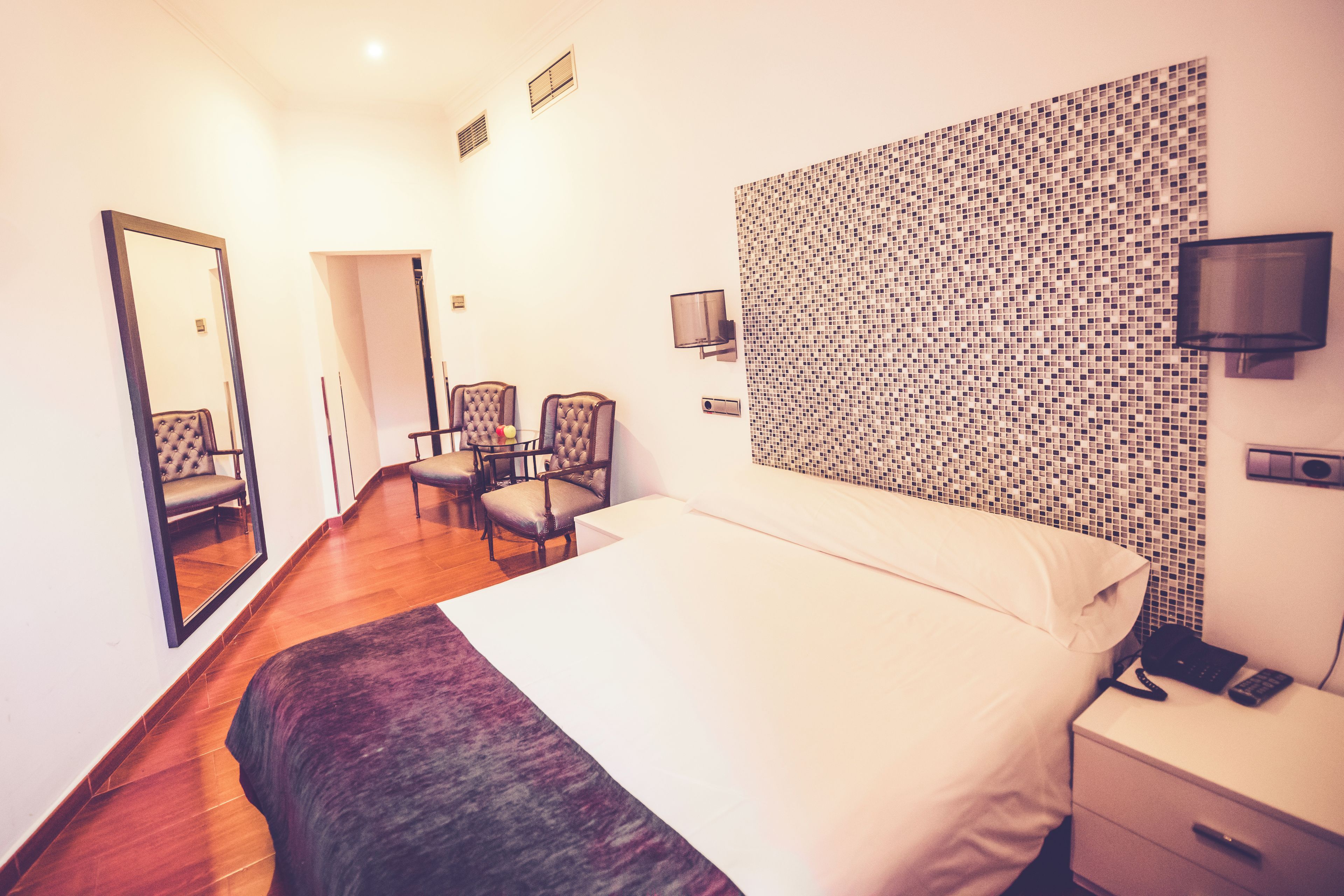 Ein Hotelzimmer mit einem großen Bett, einem Schreibtisch mit Stuhl, einem Fernseher und einer Wand mit Mosaikmuster.