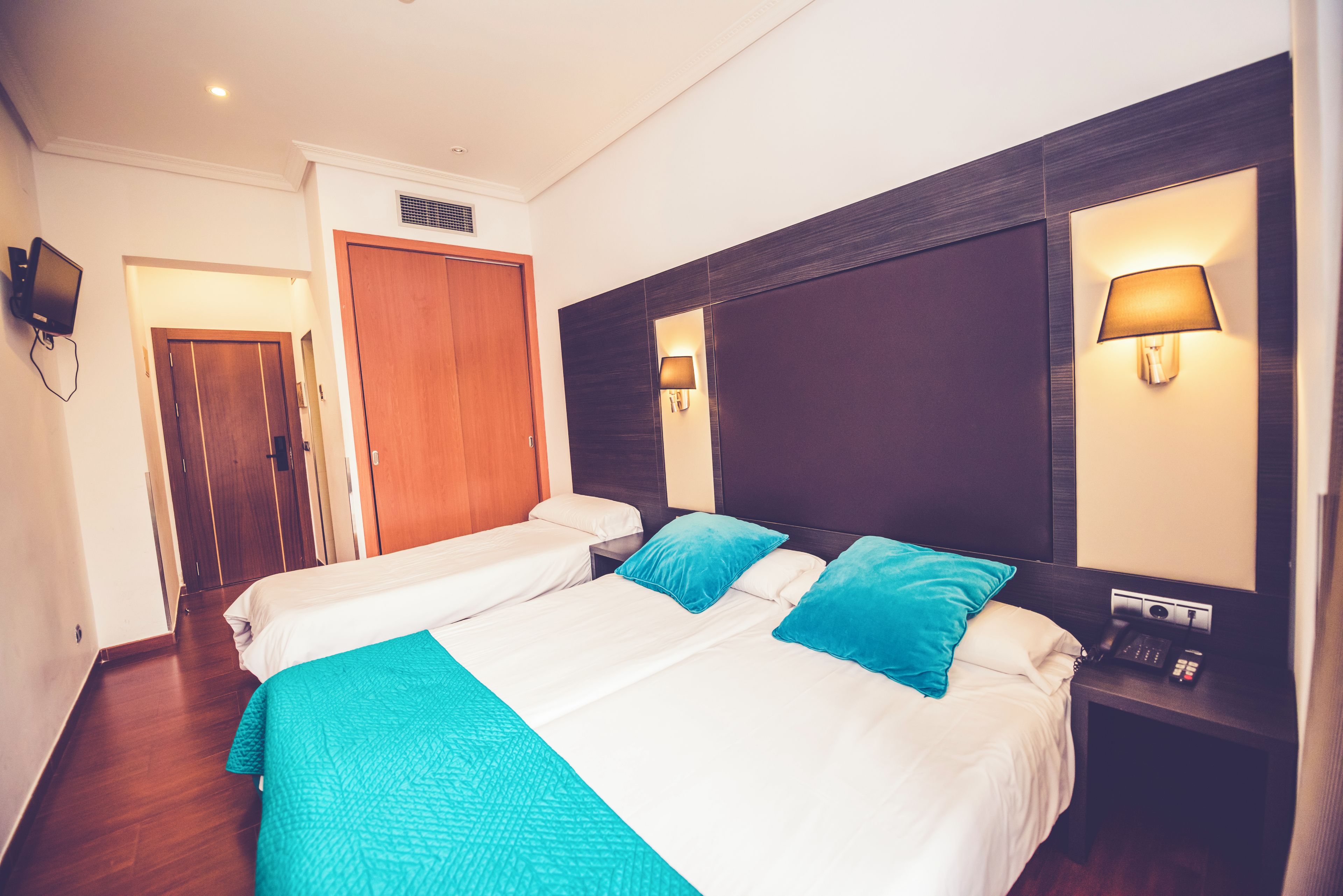 A hotel room with two beds, a wooden wardrobe, a TV, and a bedside table with a lamp and phone.
