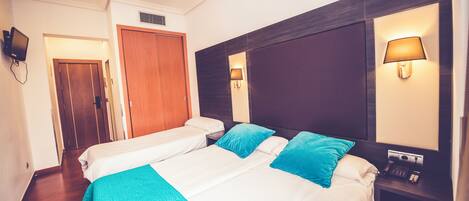 Quarto de hotel com duas camas, um guarda-roupa de madeira, uma televisão e uma mesa de cabeceira com abajur e telefone.