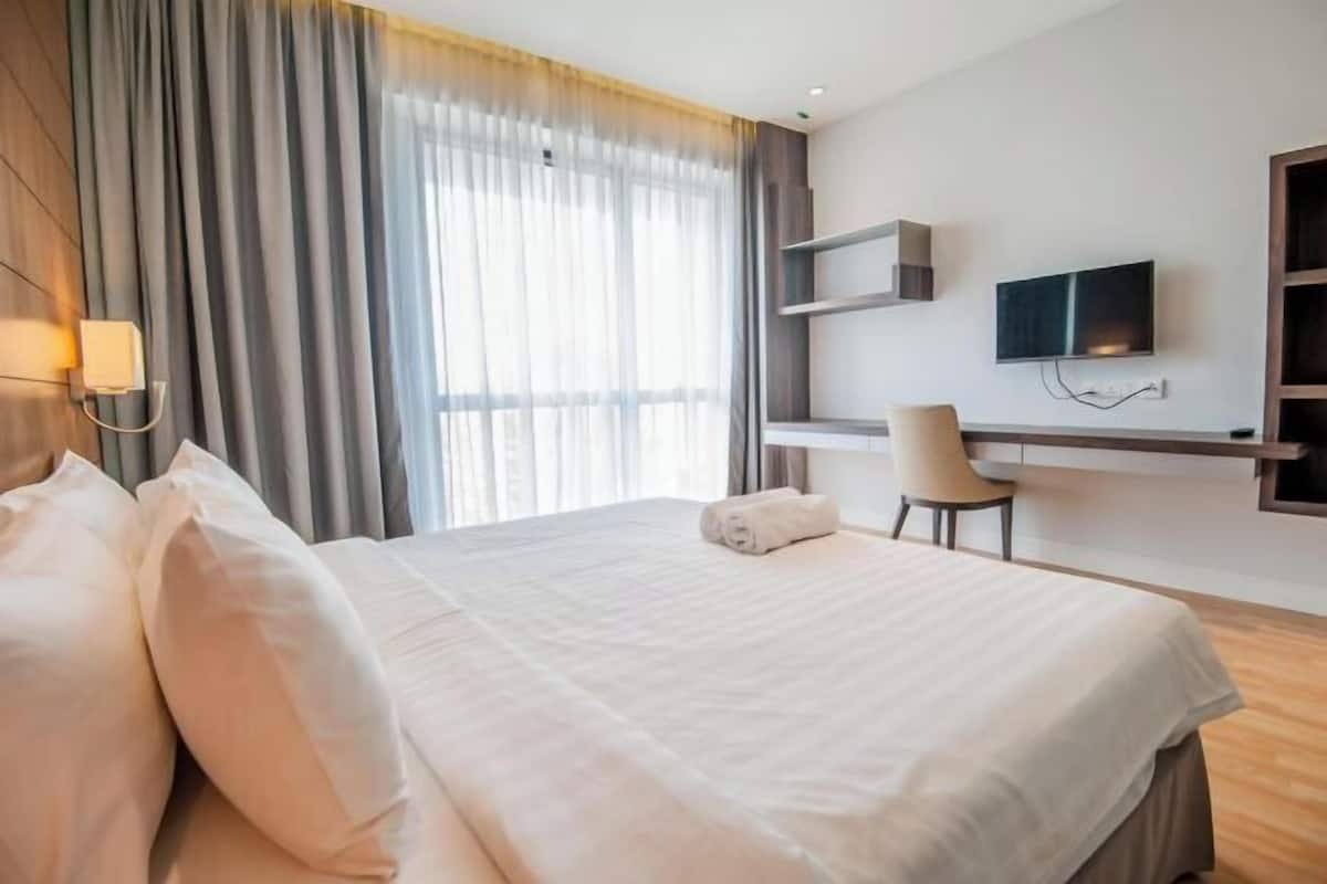 A hotel room with a large bed, a desk, a chair, a TV, and a window with curtains.
