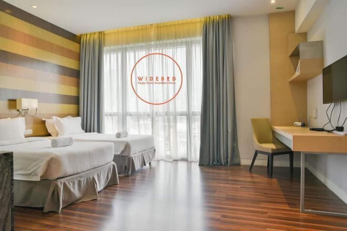 A hotel room with two beds, a desk, a chair, a TV, and a window with curtains.