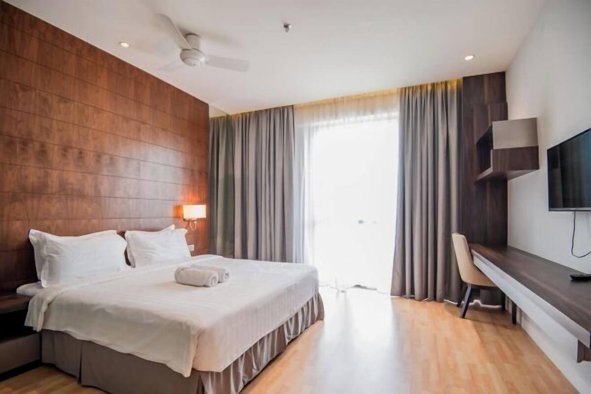 A hotel room with a bed, a desk, a chair, a television, and a ceiling fan.