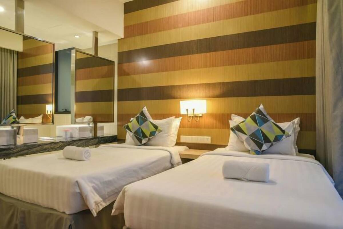 A hotel room with two beds, a large mirror, and a striped wall.
