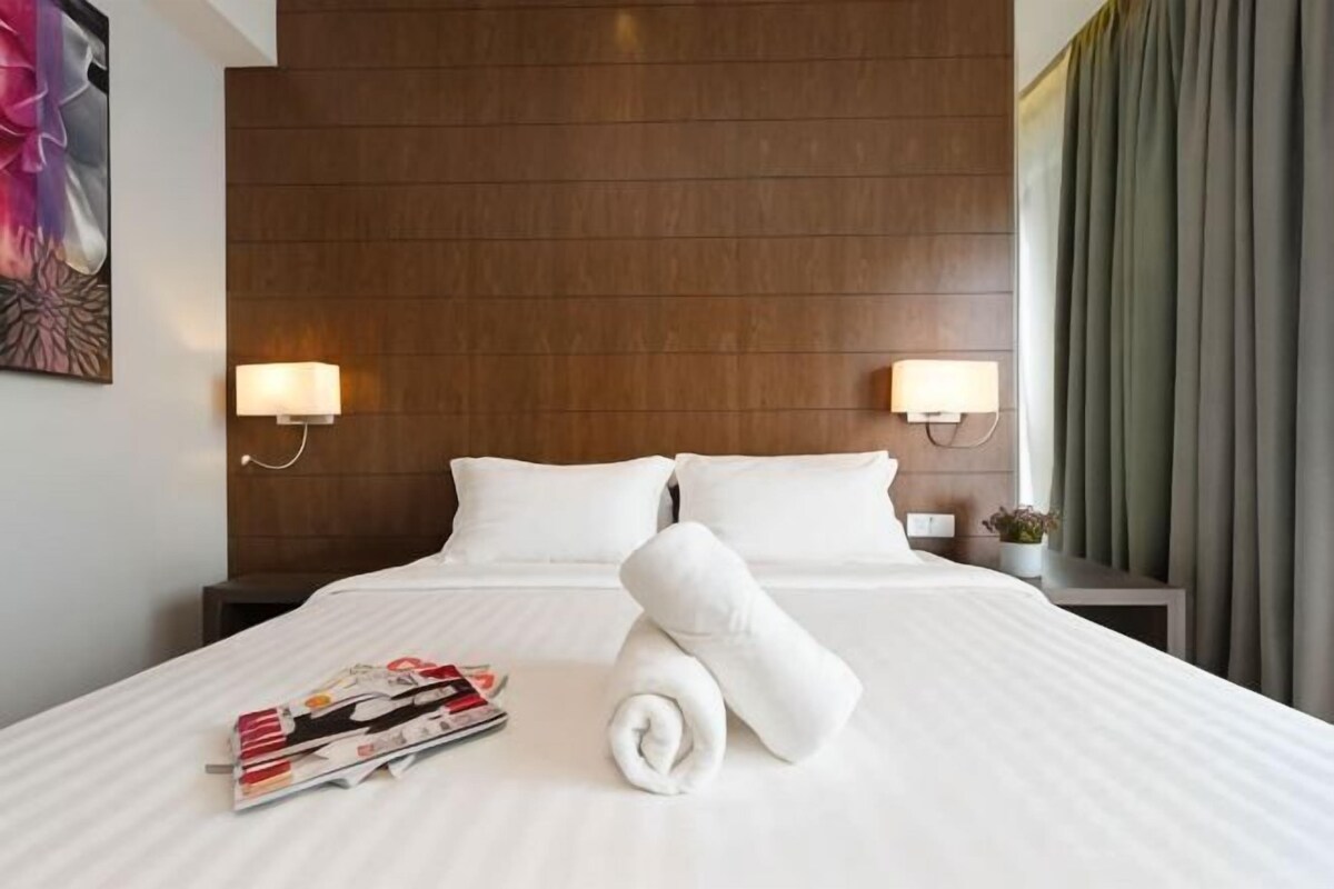 Habitación de hotel con una cama grande, dos lámparas de noche, una mesita de noche con lámpara y un ventanal con cortinas.