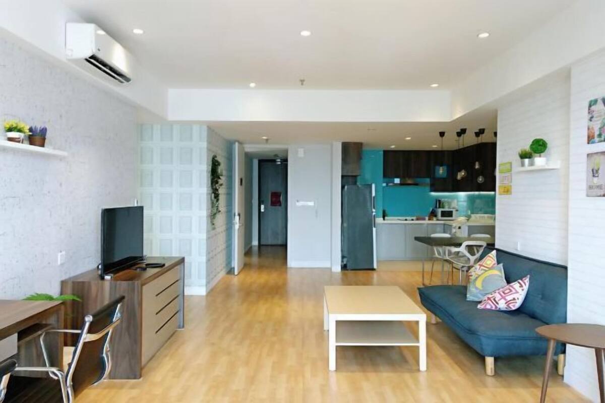 A modern living space with a wooden dining table, a sofa, a small white table, and a kitchen area with teal cabinets.