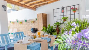 Un patio con mesas y sillas de madera azul, un muro de ladrillo, macetas colgantes y un armario de madera.