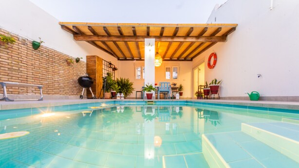 Una piscina con techo de madera y plantas en macetas alrededor.