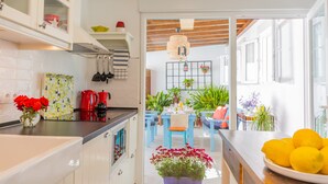 Una cocina moderna con armarios blancos, encimera negra y un hervidor rojo. Hay un comedor con sillas azules y una mesa preparada para dos personas.