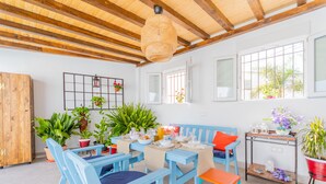 Un comedor con mobiliario azul, vigas de madera y plantas en macetas.