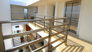 Ein mehrgeschossiges Interieur mit einer zentralen Treppe, einem modernen Aufzug und Blumentöpfen.