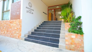 Ein Gebäudeeingang mit einem Schild, auf dem „MENSES 25 & 26“ steht, und einer Treppe, die hineinführt.