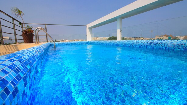 Ein Dachpool mit klarem, blauem Wasser, einer Topfpflanze und Blick auf die Stadtlandschaft.