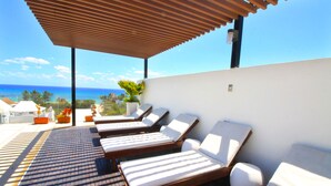 Uma área de lounge no terraço com espreguiçadeiras e vista para o oceano.