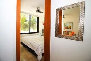 A bedroom with a bed, a window, a ceiling fan, and a mirror with a decorative frame.