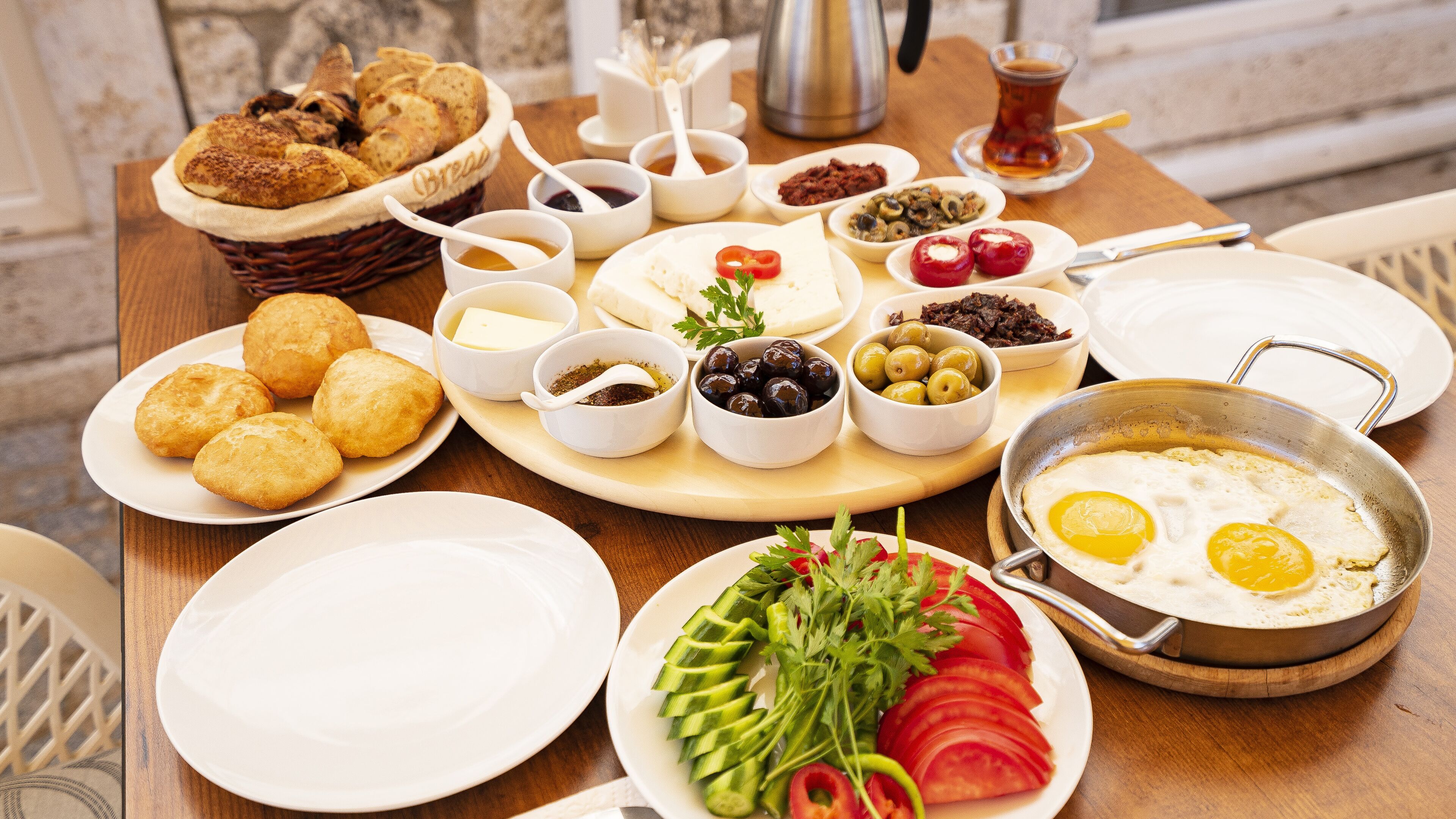 A breakfast table with various dishes including bread, eggs, olives, and vegetables.