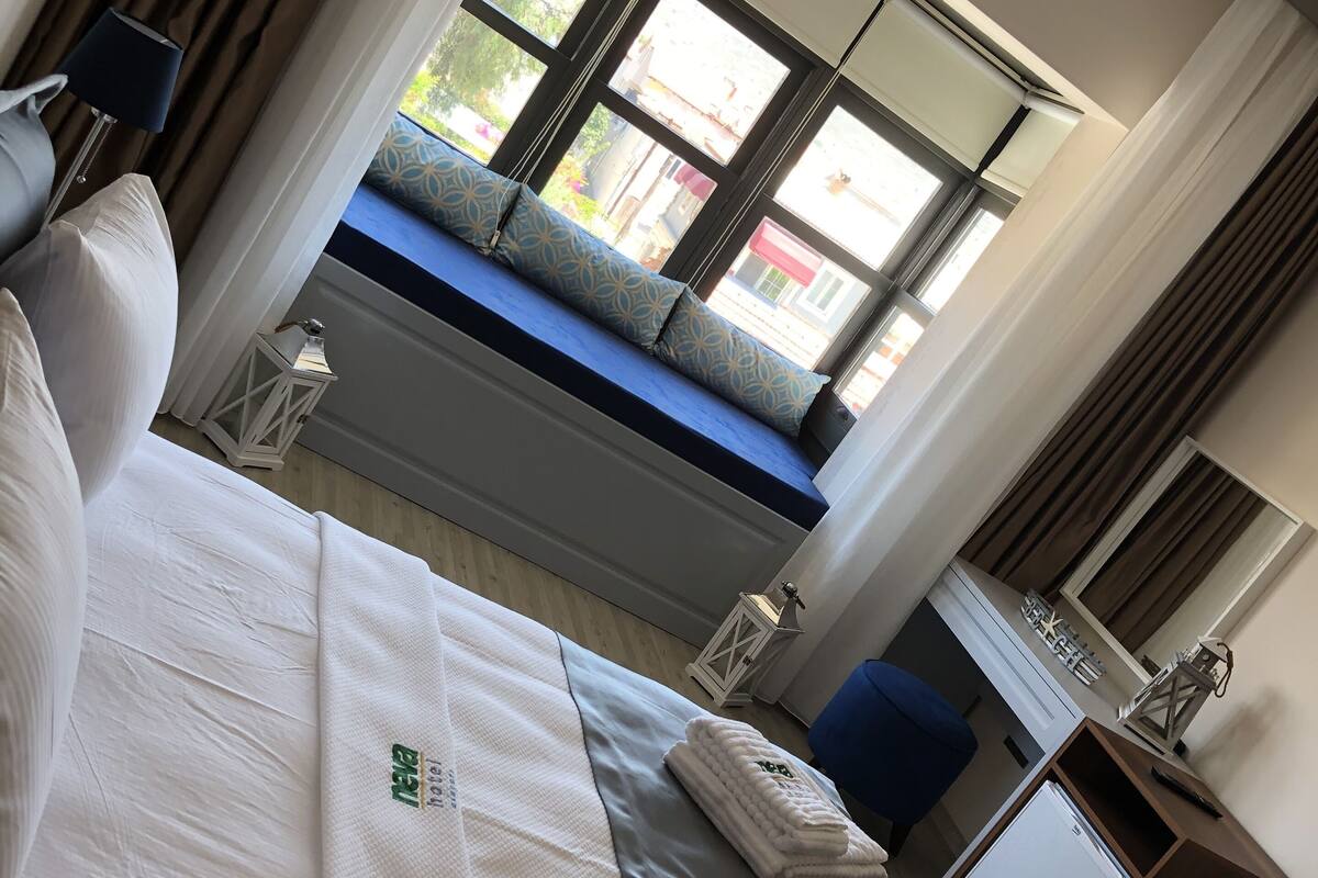 A hotel room with a bed, a window seat, a desk, and a small refrigerator.