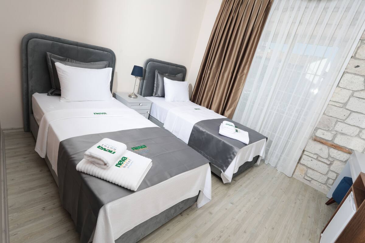 A hotel room with two beds, each with a grey headboard, white bedding, and a neatly folded towel with a logo.