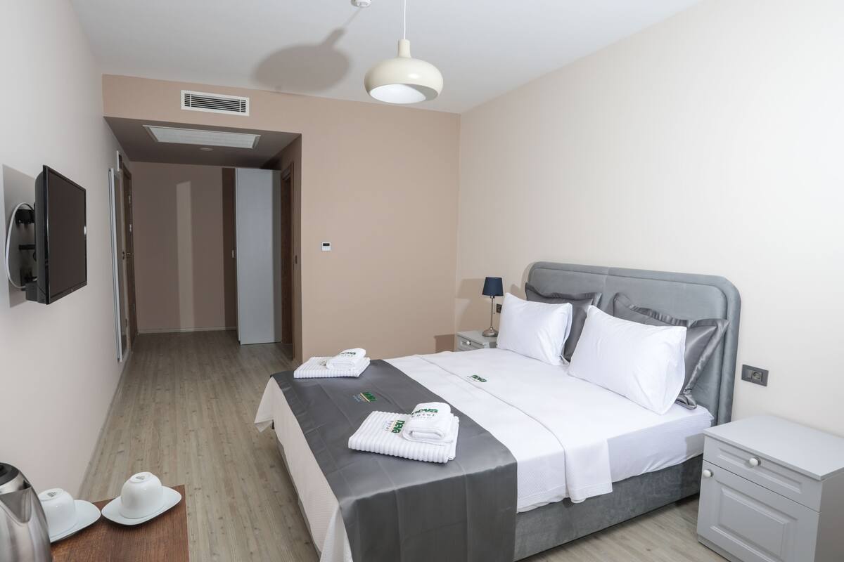 A hotel room with a bed, bedside table, and a television mounted on the wall.