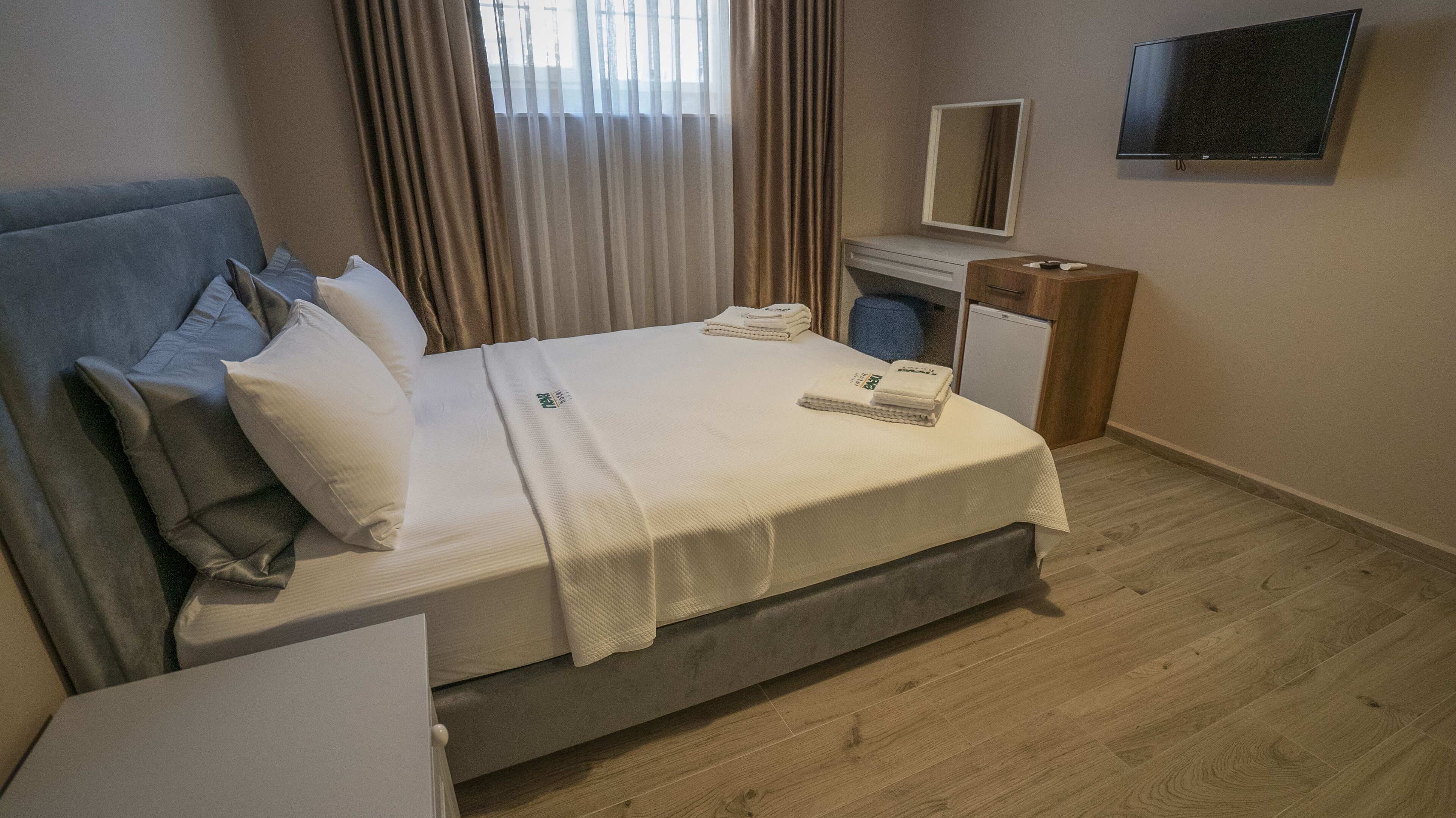 Quarto de hotel com cama, escrivaninha, cadeira, televisão e um pequeno frigorífico.