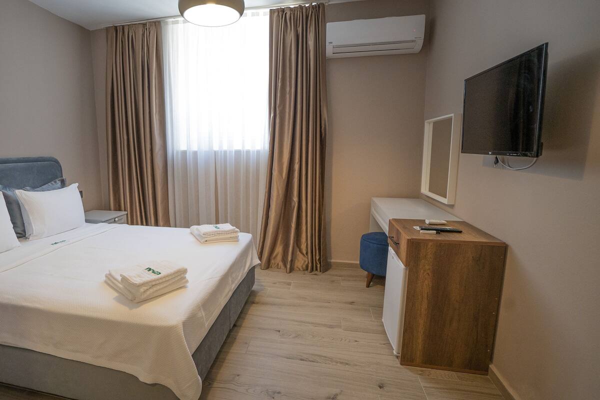 A hotel room with a bed, a desk, a TV, and an air conditioning unit.