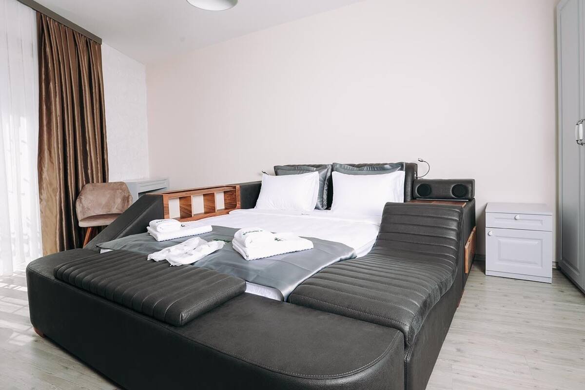 A modern hotel room with a large bed, a bedside table, a small bedside lamp, and a wardrobe.