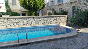 A swimming pool with stone walls and a tiled edge, surrounded by cobblestone ground. - Neva Hotel Alacati (Cesme)