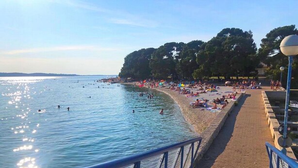 Een strand met mensen die zwemmen en zonnebaden, een heldere lucht en een hek langs het pad.