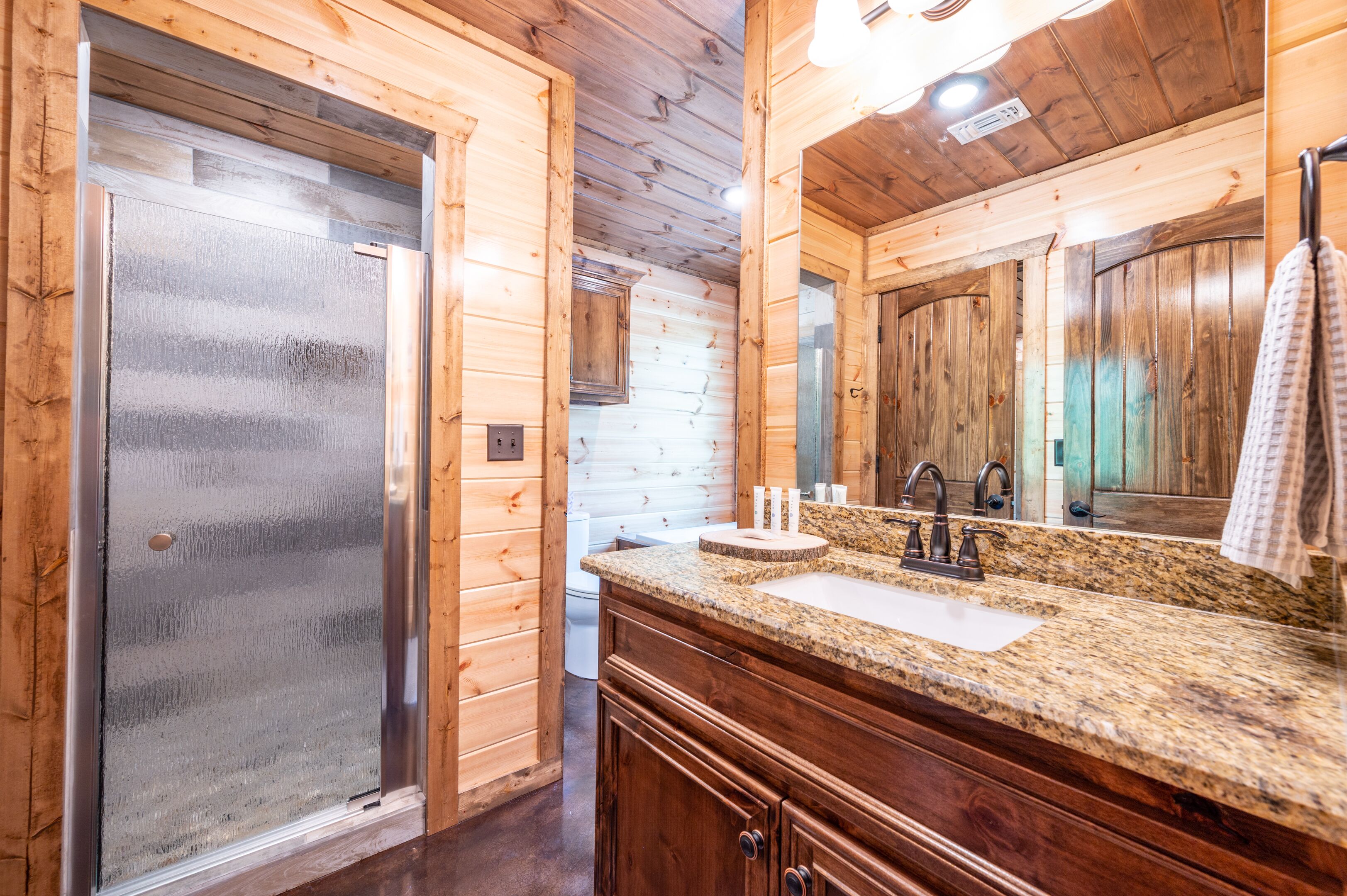 A wooden cabin bathroom with a granite countertop sink, wooden cabinets, and a large mirror.