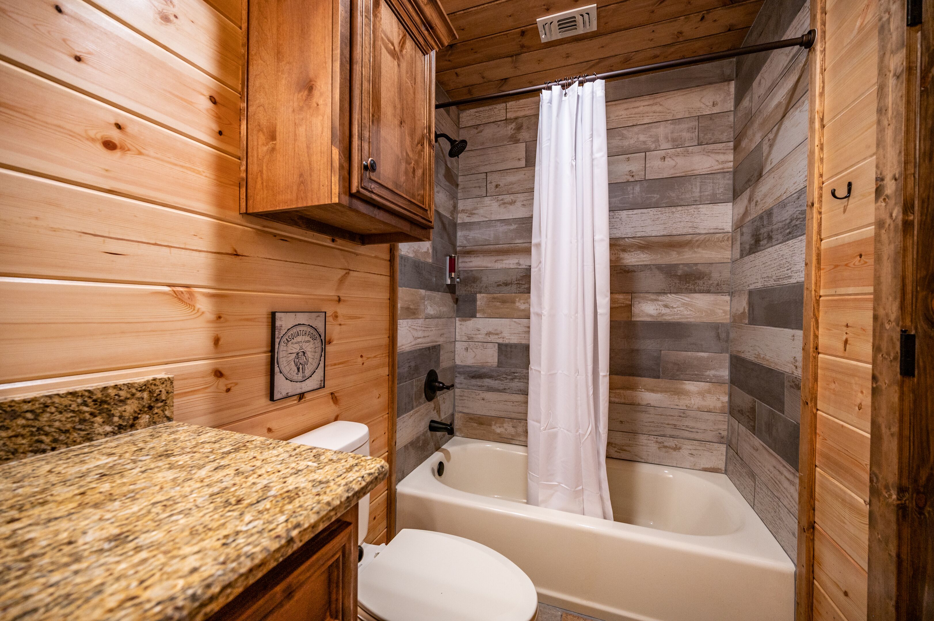A wooden cabin bathroom with a granite countertop, a toilet, and a bathtub with a shower curtain.