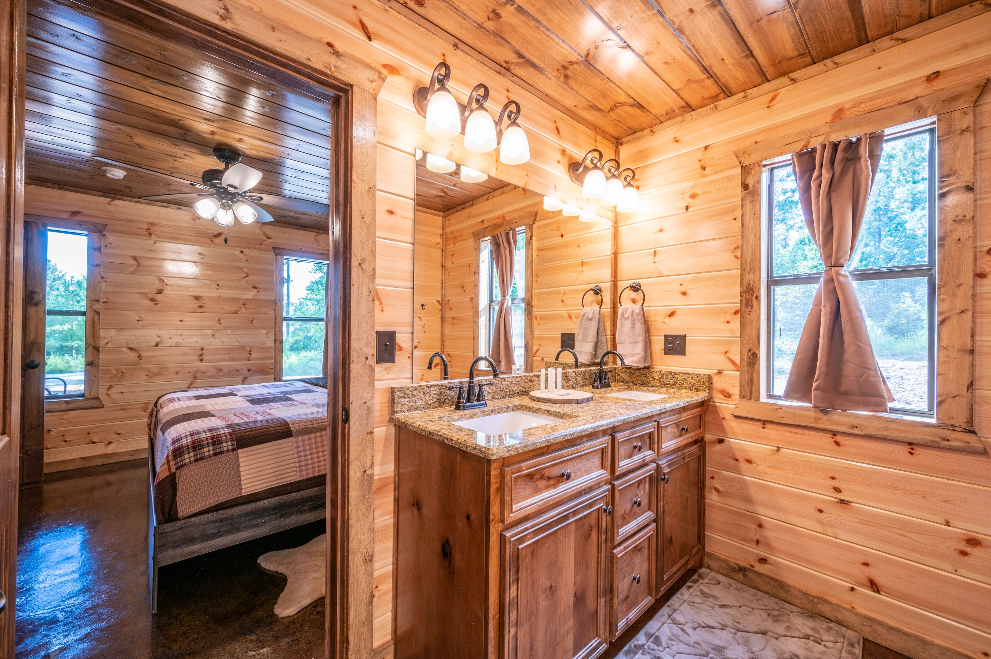 A wooden cabin interior with a bed, a bathroom with a sink and vanity, and a ceiling fan.