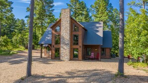 Une cabane en rondins avec une cheminée en pierre, de grandes fenêtres et une véranda couverte.