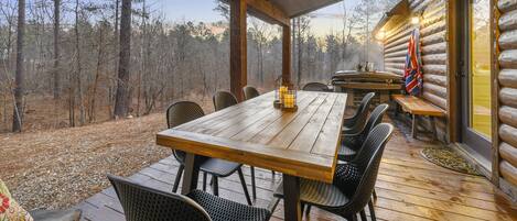 A wooden deck with a table and chairs, overlooking a forested area.