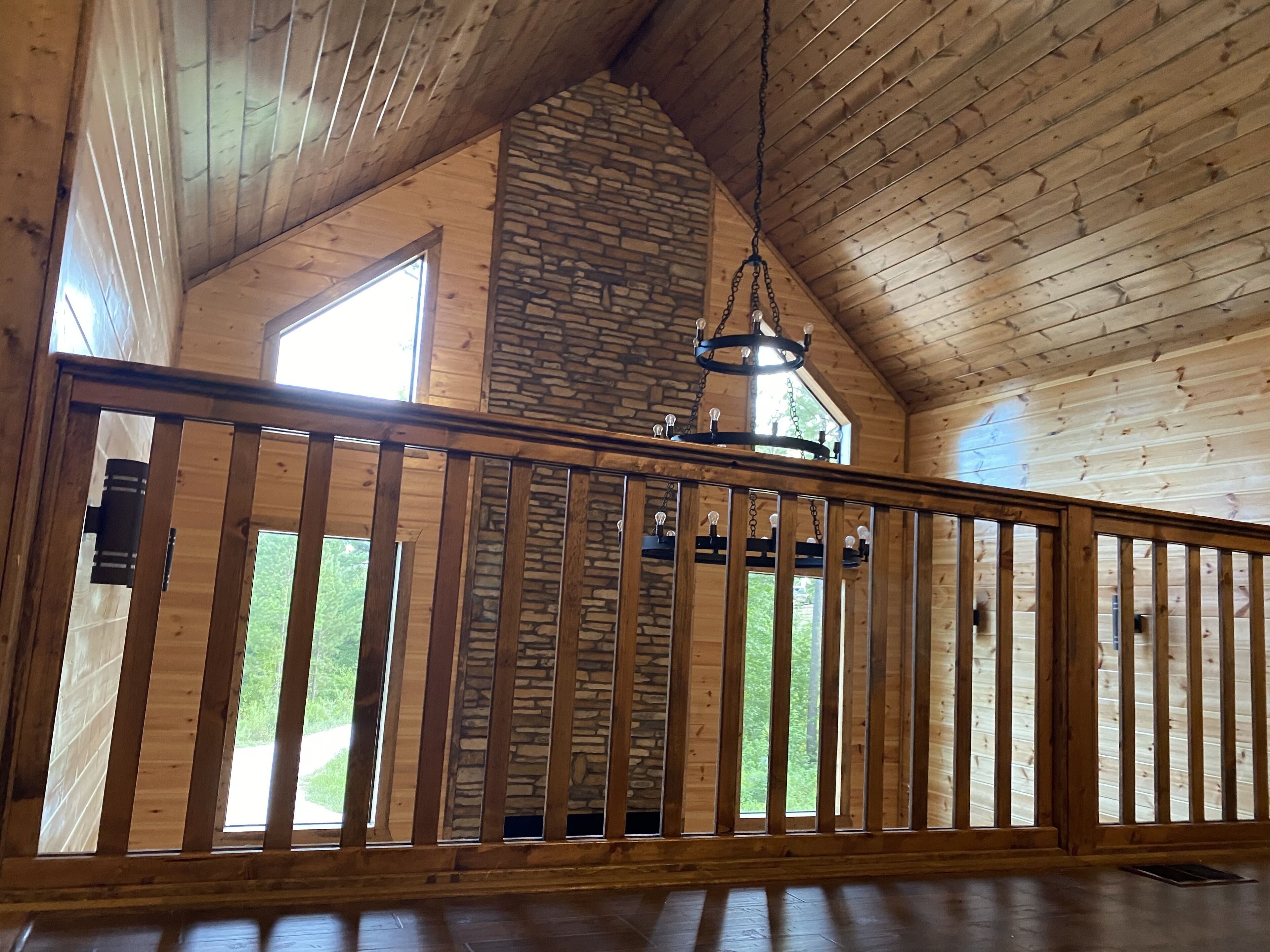 Un interior de madera con chimenea de piedra, ventanas grandes y una lámpara colgante.