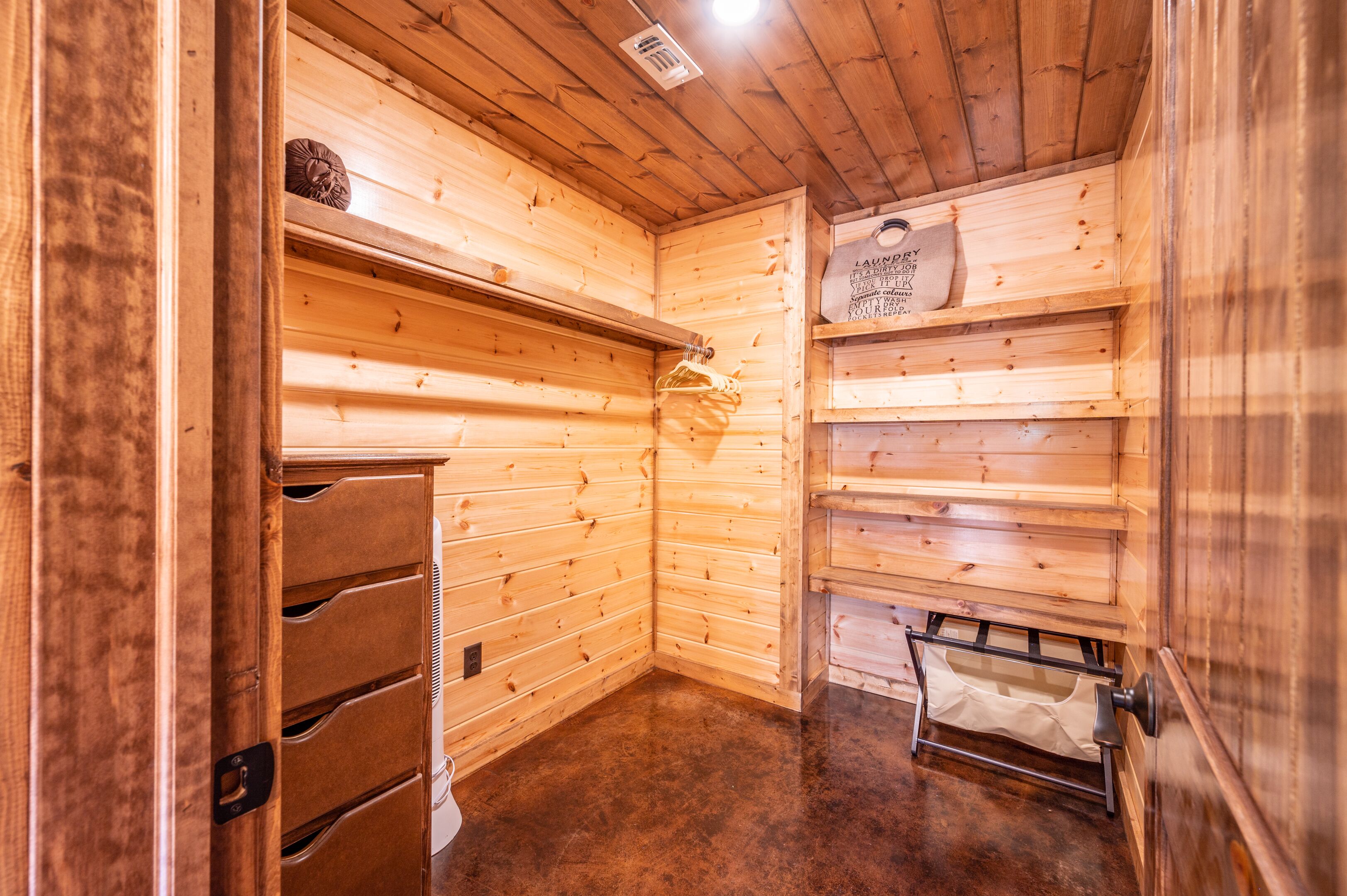 Un intérieur en bois avec un chauffage intégré, un étendoir et une étagère sur laquelle est accroché un panneau indiquant qu'il s'agit d'une buanderie.