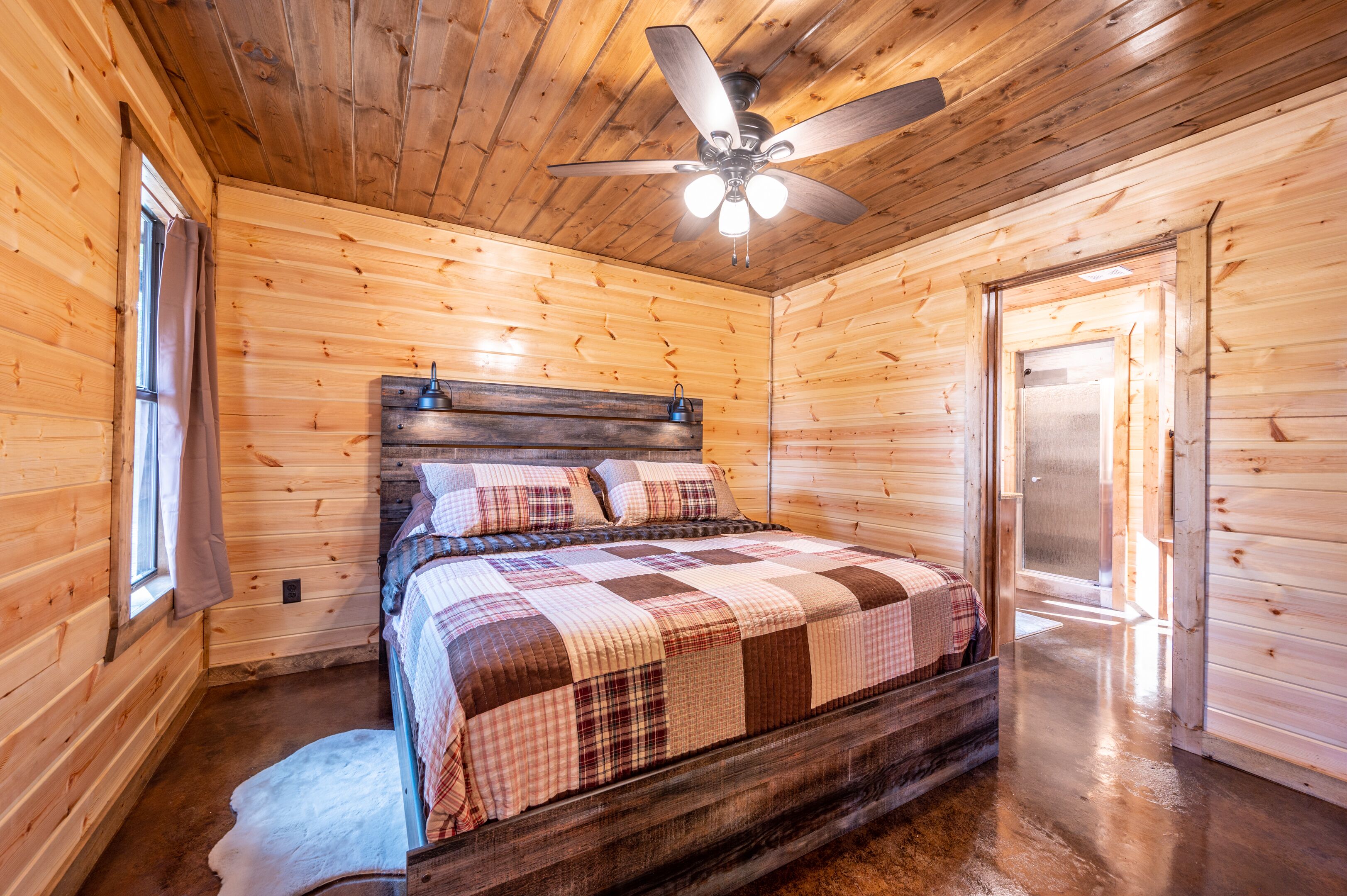 A wooden cabin bedroom with a bed, a ceiling fan, and a door.
