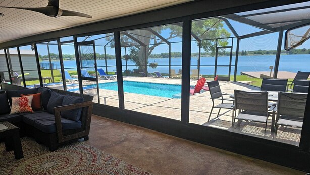 A room with a large window overlooking a pool and lake. There is a sofa with cushions and a patterned rug on the floor. - Family Home on Bellows Lake, with new pool.  6505 Walton Way (Tampa)