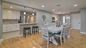 A modern kitchen with white cabinets, a stainless steel refrigerator, and a dining area with a white table and chairs. - Family Home on Bellows Lake, with new pool.  6505 Walton Way (Tampa)