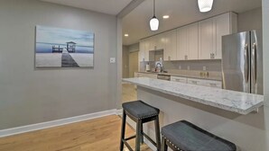 A modern kitchen with a marble countertop, stainless steel appliances, and a painting of a pier on the wall. - Family Home on Bellows Lake, with new pool.  6505 Walton Way (Tampa)