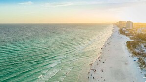 A beach with a long stretch of sand, a few people, and buildings in the background.