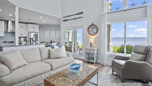 A spacious living room with a large window, a sofa, a coffee table, and a view of the ocean.