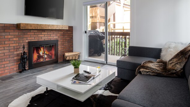 A modern living room with a fireplace, a flat-screen TV, a sofa, and a sliding glass door to the outside. - Outpost: Sleeping Indian W5 (Teton Village)